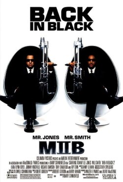 Two men in black men, sitting in egg-shaped chairs, holding large guns