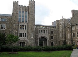 Four-story tower on left with an arched walkway in the center and pedestrian bridge connecting the tower to three-story Gothic building