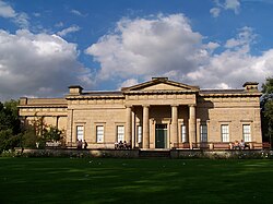 Stone block building with columned portico and large wing extending behind.