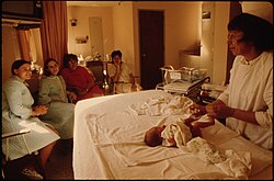 A group of women look on as a nurse demonstrates caring for an infant on a hospital bed