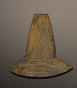 Photo of a metallic object shaped as an axe-head. It has brown irregular surface and rests on a black plate.