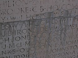 Names carved into a wall are covered in unidentified mineral deposits. Many of the names are no longer readable or are heavily distorted.