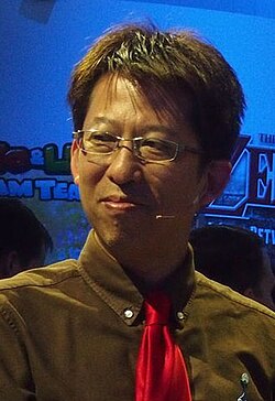 Headshot of a 50-year-old Japanese man with black-brown hair in a brown suit with a red tie, smiling away from the camera