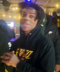 A young Black man looking at the camera smirking in a public place.