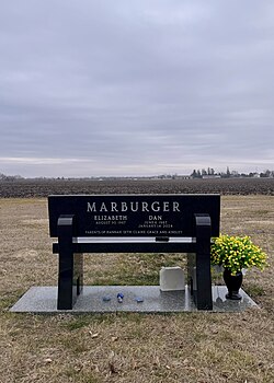 A grave marker in the shape of a bench, with Dan Marburger and his wife engraved in the stone. The bench is in Violet Hill Cemetery, 1.6 miles (2.5 kilometers) from Perry High School.