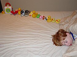 Sleeping boy beside a dozen or so toys arranged in a line
